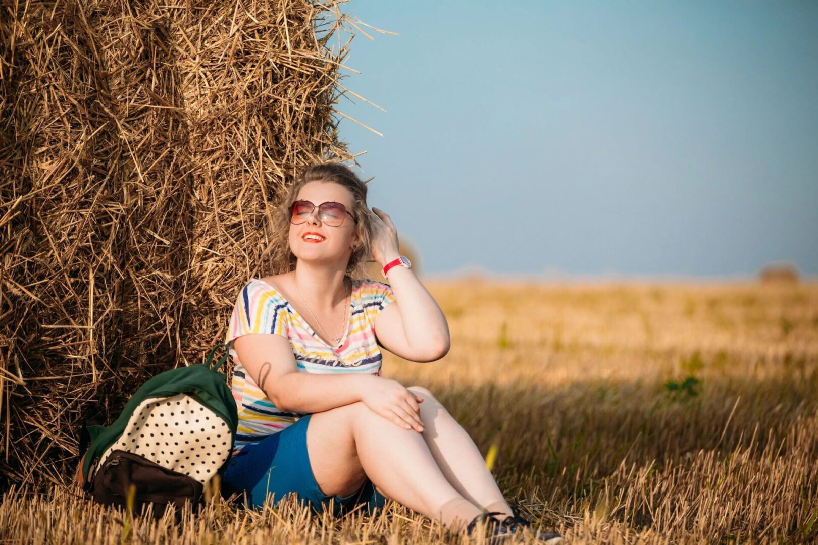 A woman sitting in the grass near hay bales.