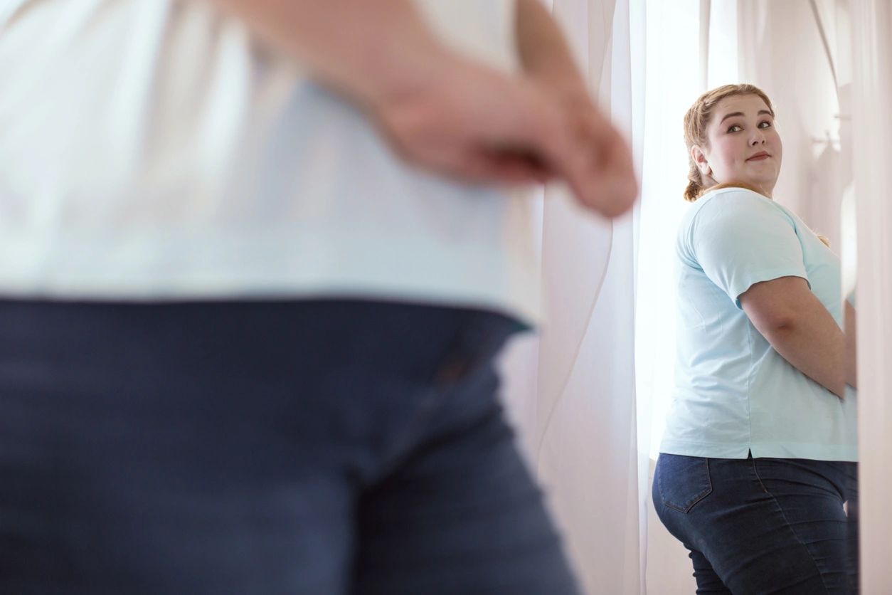 A woman standing next to another person in front of a window.